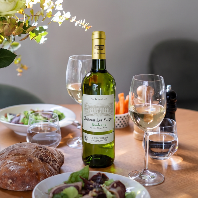 Château Les Vergnes Blanc AOP Bordeaux sur une table accompagné d’une salade