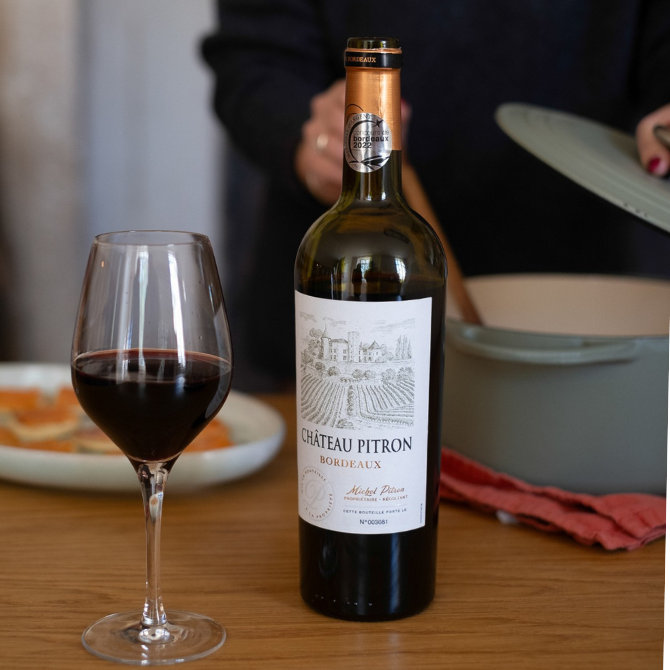 Château Pitron Rouge AOP Bordeaux sur la table de la cuisine avec préparation de repas en arrière-plan