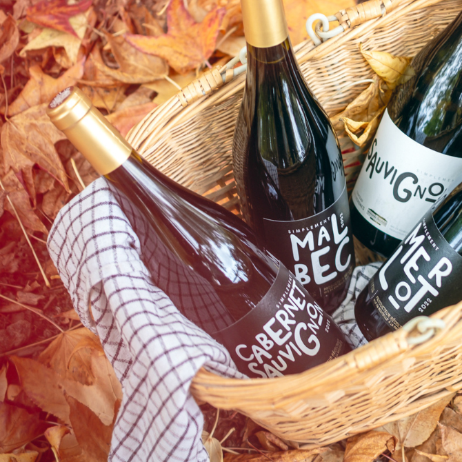 Bouteilles de la collection Simplement Cépages, dont Simplement Cabernet Sauvignon, dans un panier sur un tapis de feuilles d’automne